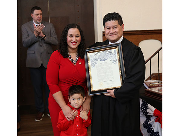 Jason Luong holding a framed document with his wife and son